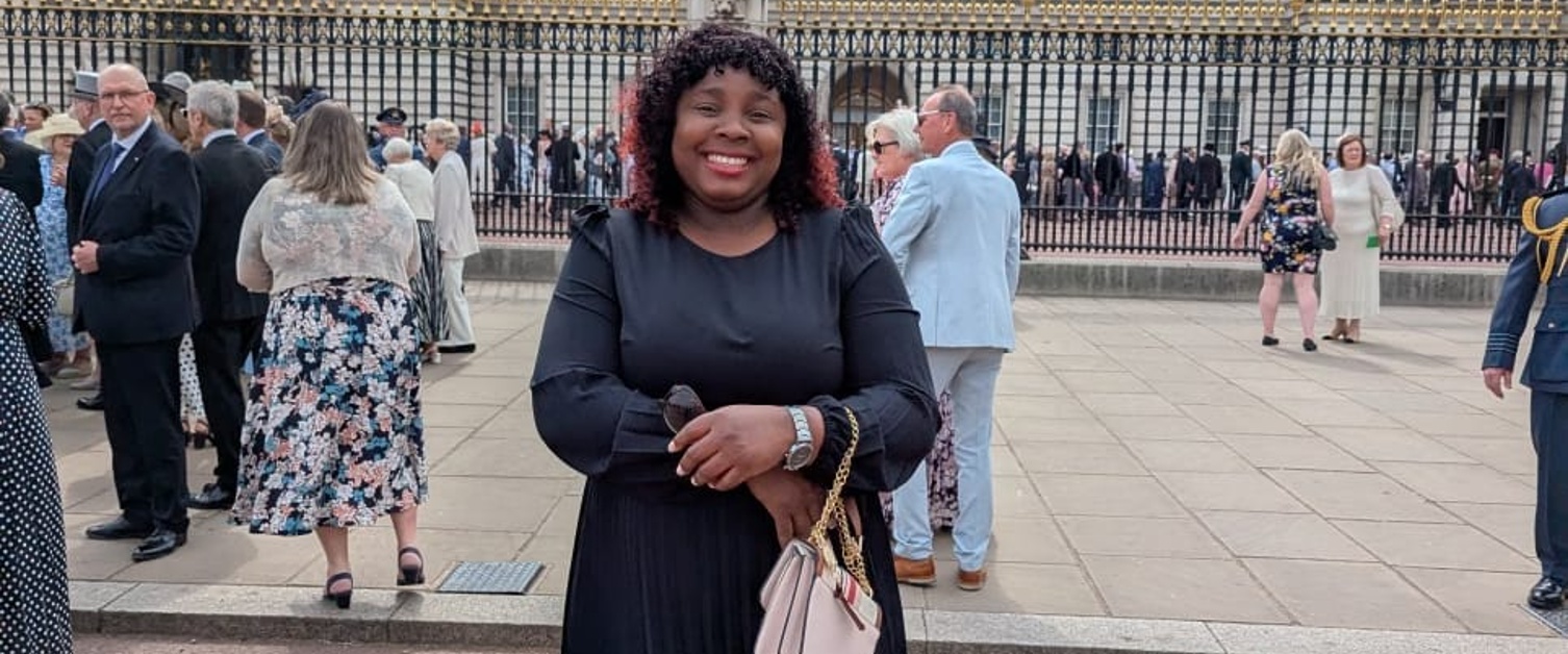 Image shows a woman standing in front of Buckingham Palace