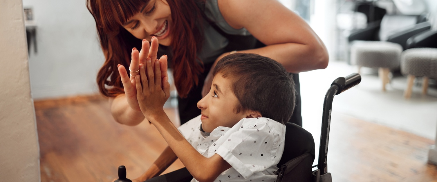 Child in a wheelchair high fiving an adult. Both are smiling.