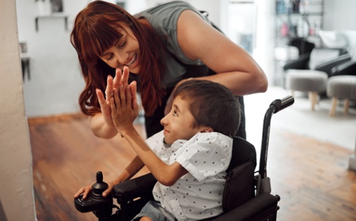 Child in a wheelchair high fiving an adult. Both are smiling.