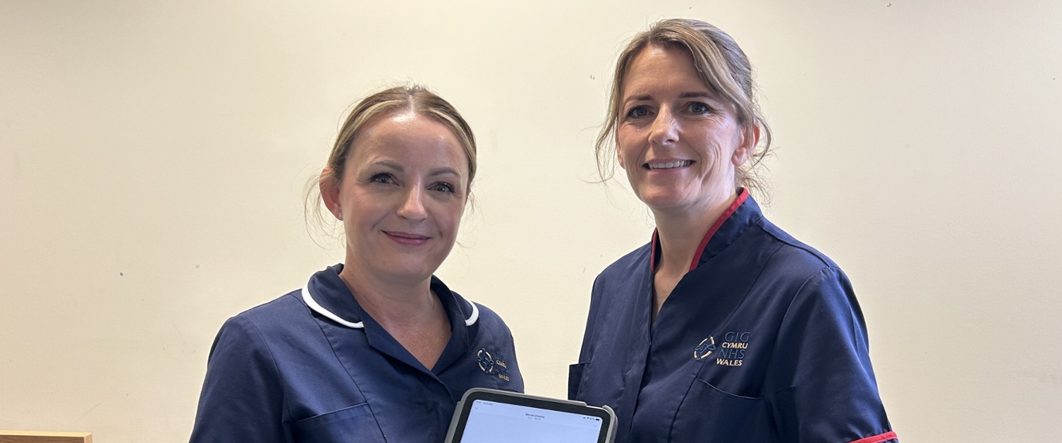 Karly holding an iPad displaying the app stood next to Catrin