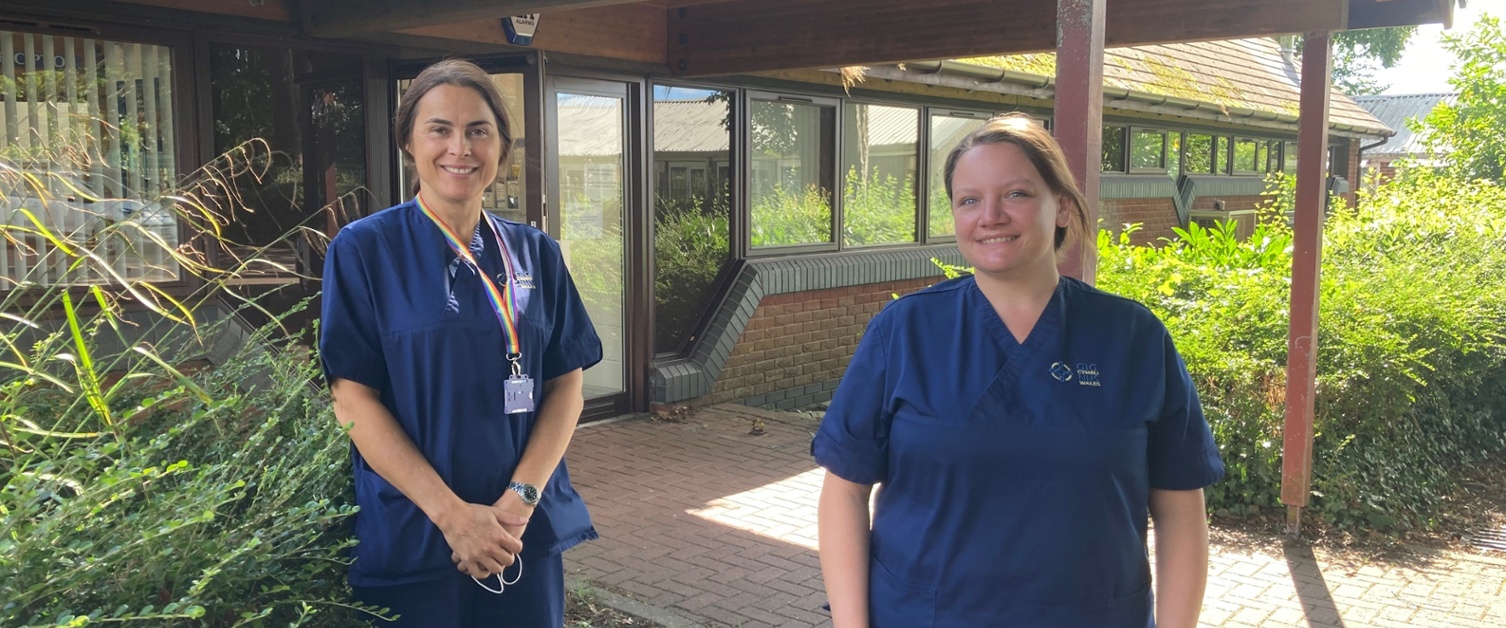 Two women wearing scrubs standing outside