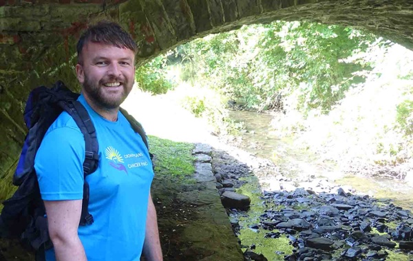 Image shows a man standing by a canal bridge.