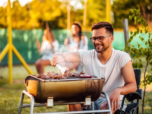 Image shows a man next to a barbeque