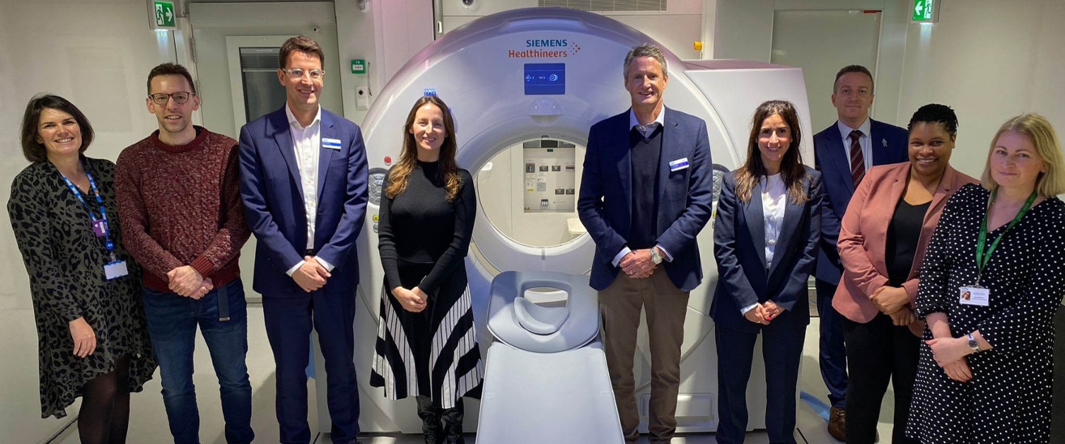 Image shows a group of people standing either side of a medical scanner