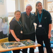 Senior radiographer Tracy Lewis stands with patient Michael Puffett and radiographer Rebecca Lloyd next to the puzzle table.