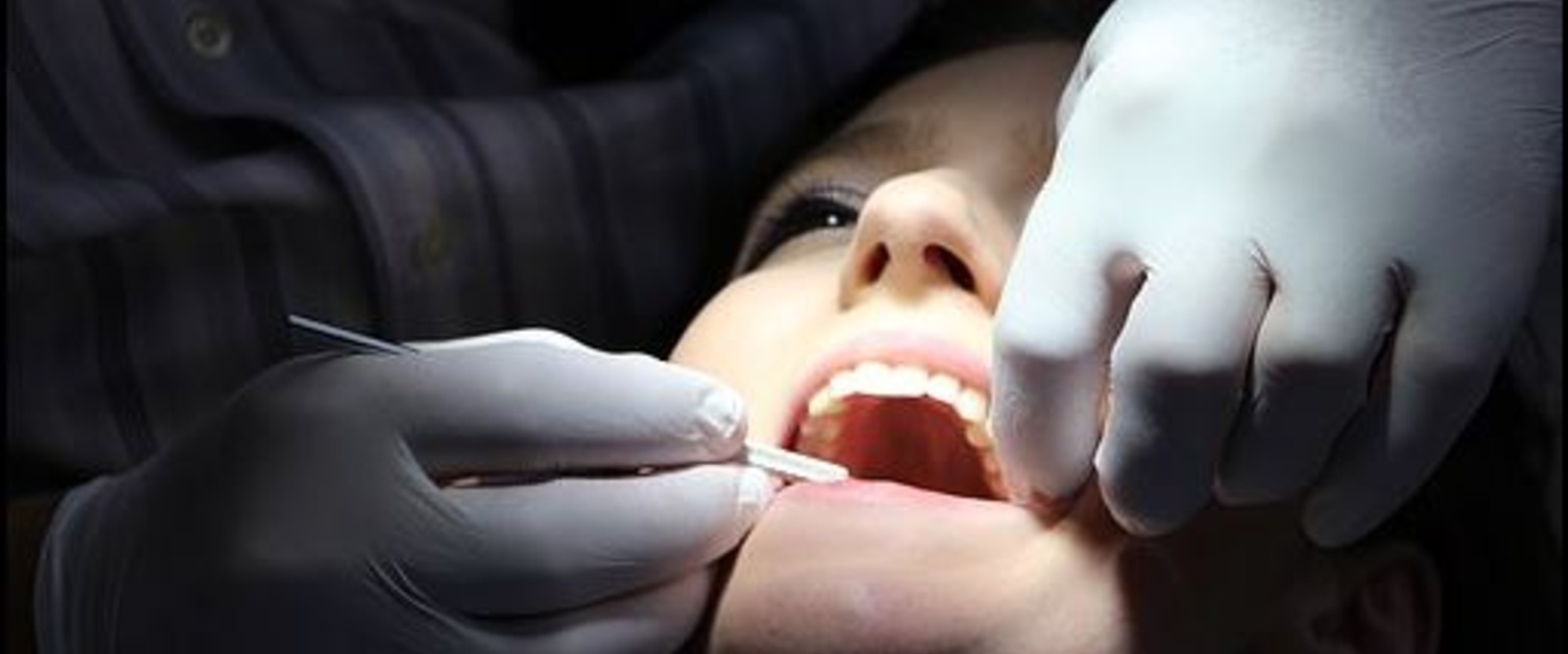 A woman with her mouth open is examined by a dentist.