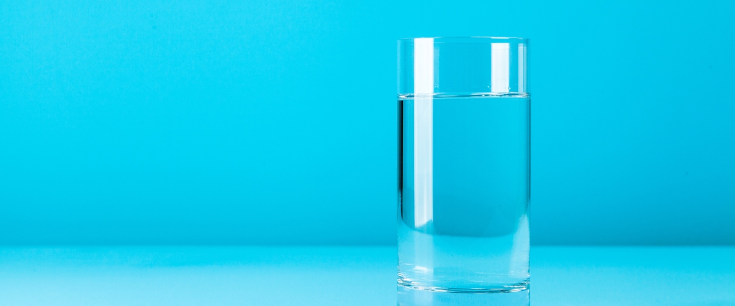 Image shows a plain glass of water on a table against a blue background.