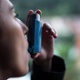 Image shows a woman using an inhaler