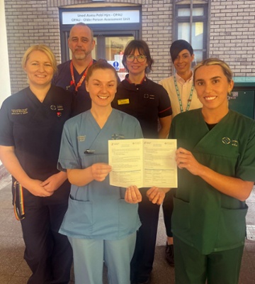 Image shows a group of clinicians and two female staff holding a leaflet