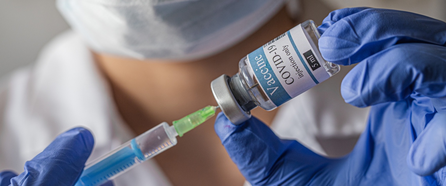 A health care worker wearing a mask and gloves fills a syringe with Covid vaccine.