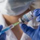 A health care worker wearing a mask and gloves fills a syringe with Covid vaccine.