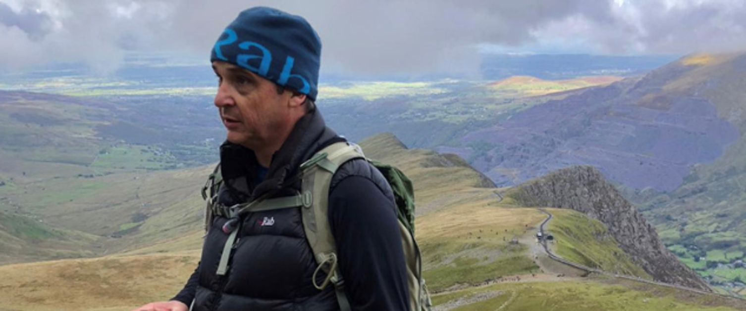 Image shows a man walking in a mountain setting.