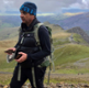 Image shows a man walking in a mountain setting.