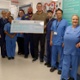 A group of nursing staff standing alongside a man holding a large cheque.