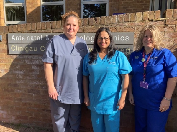 Three women in scrubs stood outside a hospital
