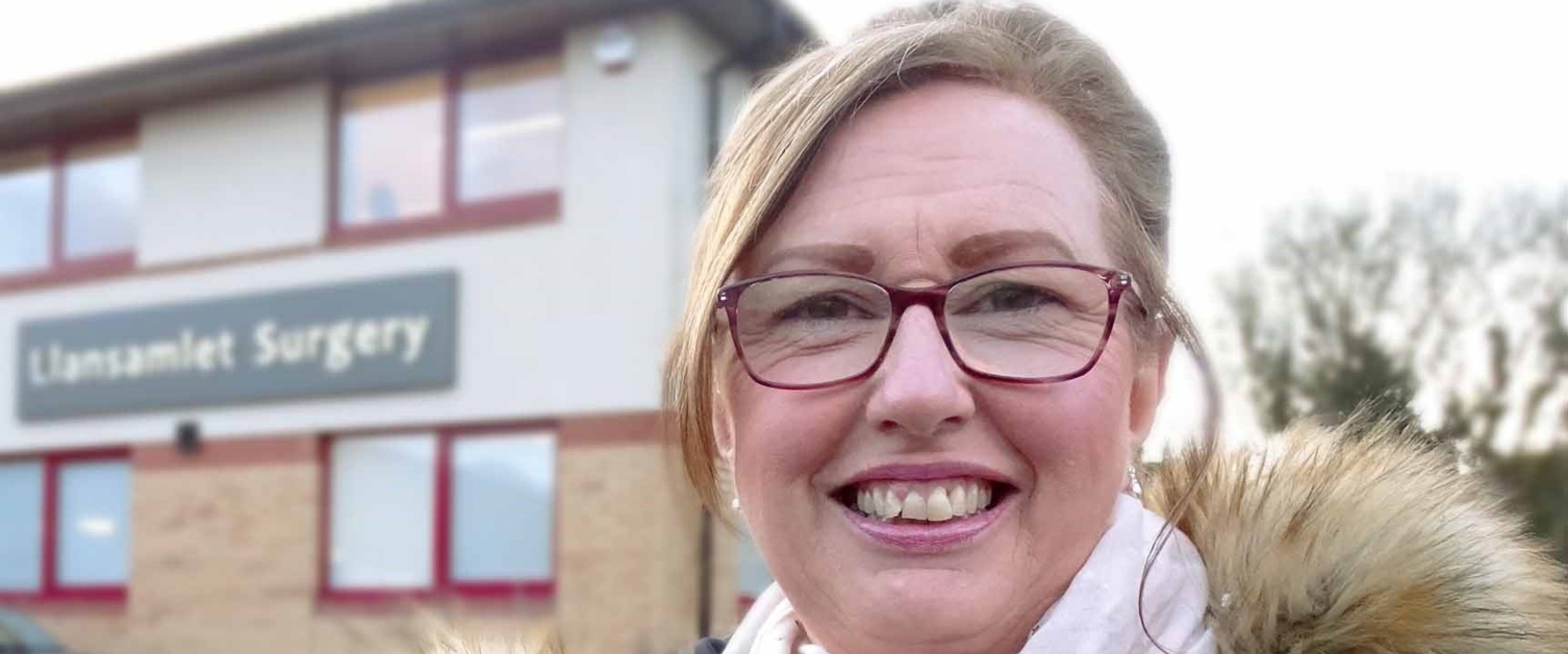 A smiling Anne Robinson standing outside her local GP surgery.