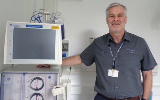 Image shows a man standing alongside a dialysis machine.