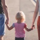 Image shows a child holding hands with parents.