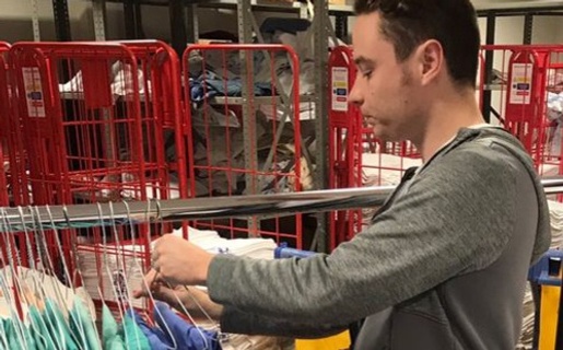 Project SEARCH intern Kieran Jones hands fresh scrubs on a rail in the linen room at Morriston Hospital.