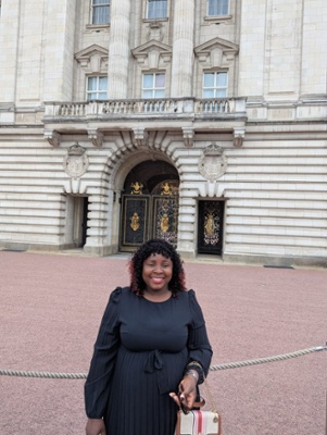 Image shows a woman standing in front of Buckingham Palace