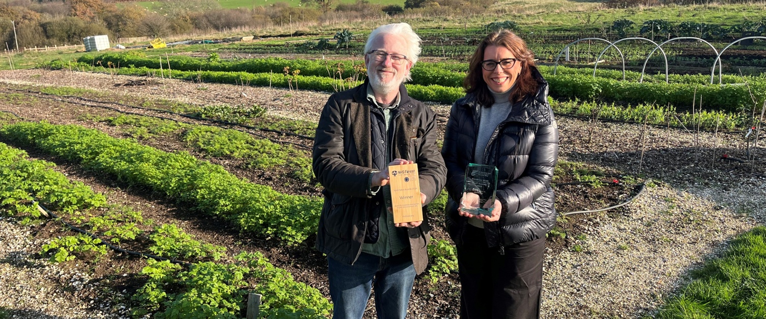 Image shows a man and woman holding awards in a field