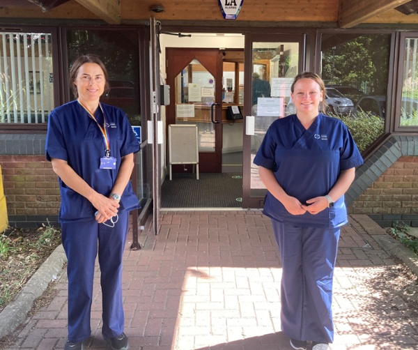 Two women wearing scrubs standing outside a GP practice