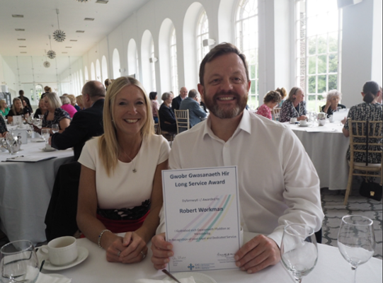 Image shows woman sitting next to a man holding a certificate