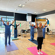 Staff members stand on mats with arms above their heads pulling a resistance band.