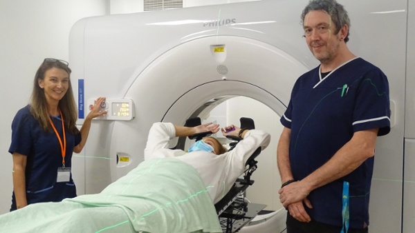 Image shows two staff members and a patient in a CT scanner room