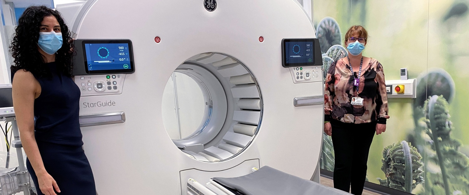 Two clinicians in surgical masks standing alongside a scanner