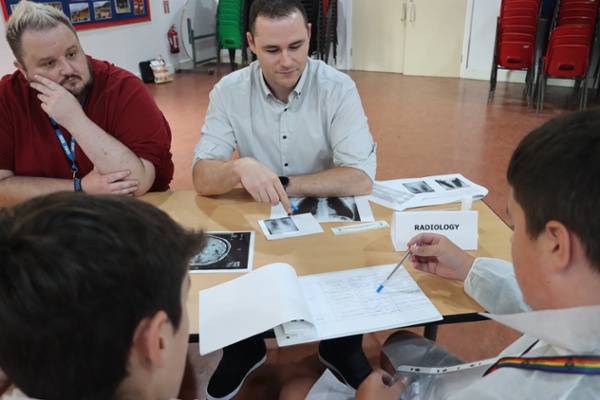 A scientist pointing to an X-Ray with a child writing notes on a worksheet