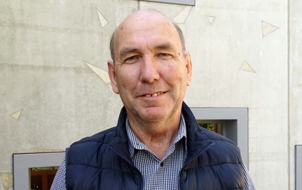 Image shows a man outside a hospital building, smiling into the camera