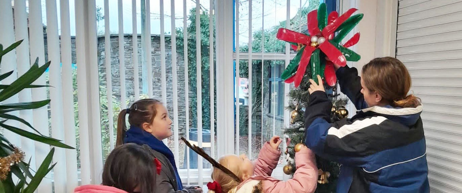 Pupils and an adult decorate a Christmas tree in Ty Olwen Hospice.