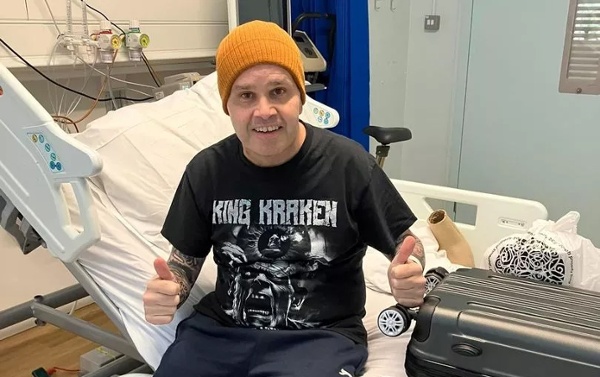 A man sitting on a hospital bed, making a thumbs-up gesture