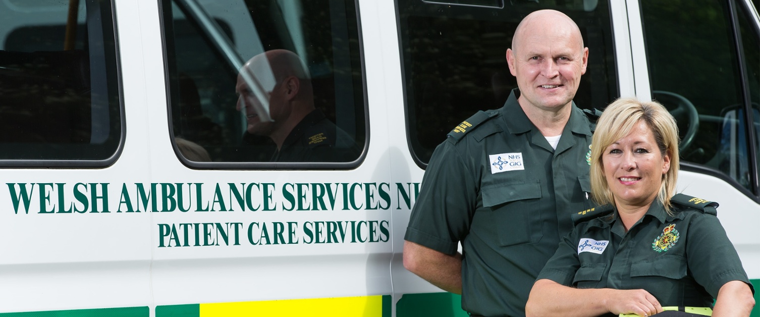 Image shows two Welsh ambulance staff next to a patient transport vehicle.