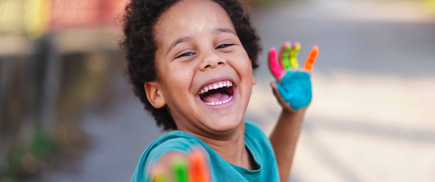Image shows young child with paint on his hands laughing at the camera.