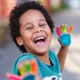 Image shows young child with paint on his hands laughing at the camera.