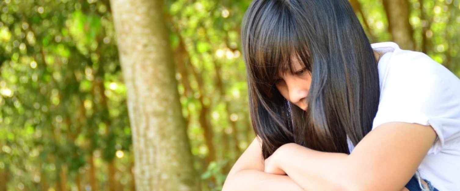 A woman sat with her arms over her knees in front of trees.