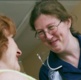 A nurse in a blue uniform smiles down at a patient with red hair.