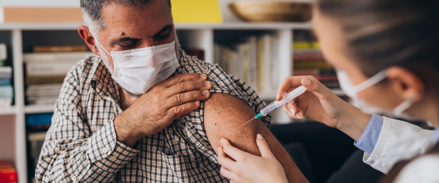 A man wearing a face covering is being given his COVID-19 vaccination by a GP.