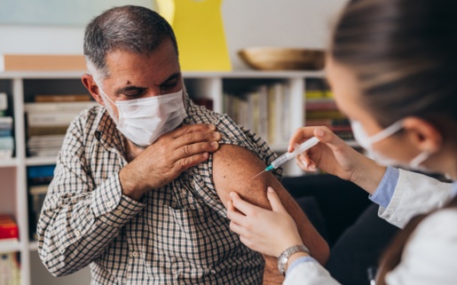 A man wearing a face covering is being given his COVID-19 vaccination by a GP.