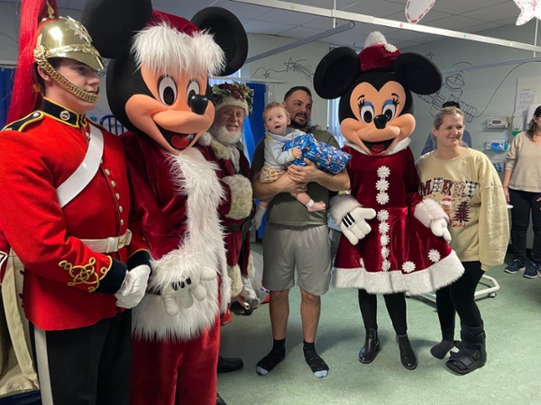 Mickey and Minnie Mouse, standing alongside a family and baby