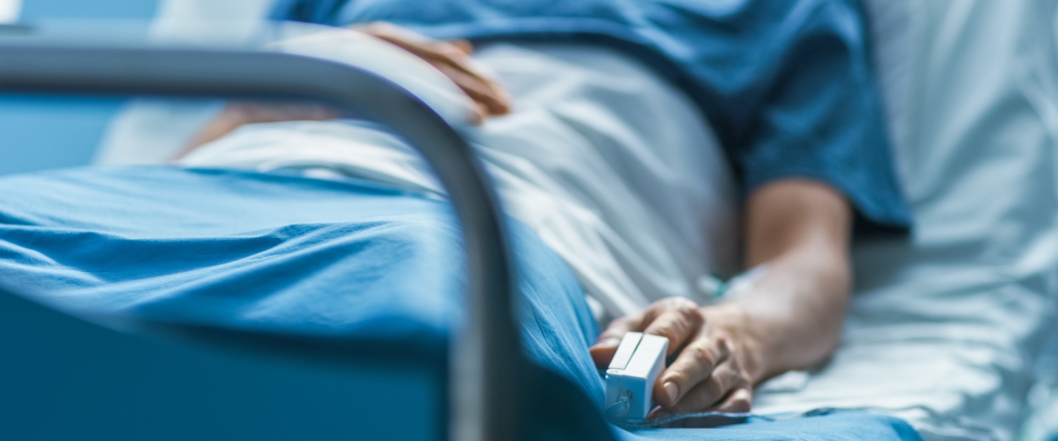 A patient lies in a hospital bed with a blood pressure monitor on their finger.