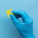 A hand in a clinical glove holds a small toy jet plane.