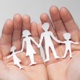 Hands hold a paper cut out in the shape of a family.