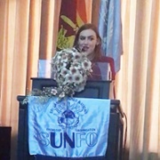 Image shows a woman speaking from behind a podium.