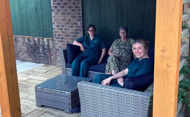 Image shows three women sitting on garden furniture