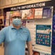 A man wearing a mask and standing in front of a noticeboard