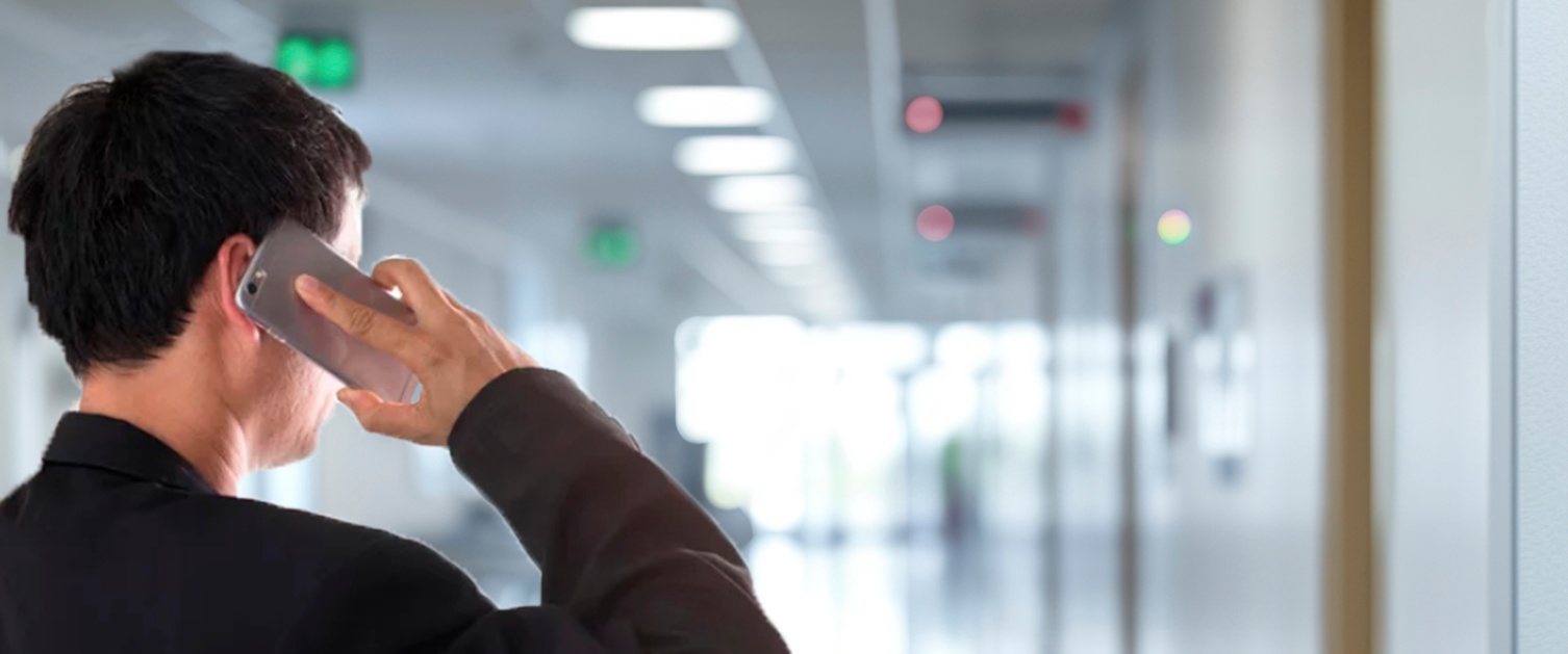 A man on the phone in an empty hospital corridor, facing away from the camera.