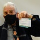 Image shows a man wearing a face mask holding up his vaccination card.